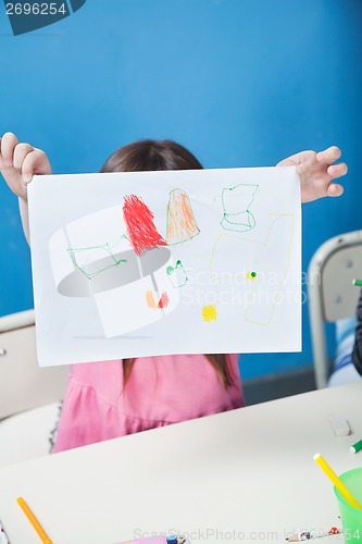 Image of Girl Holding Drawing Paper In Front Of Face In Classroom