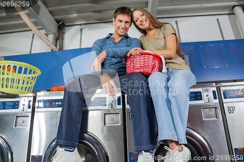 Image of Couple With Clothes Basket Sitting On Washing Machine