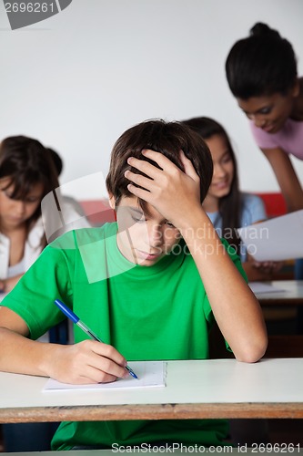 Image of Sad Teenage Boy Writing Paper At Desk