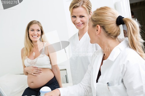 Image of Doctors Looking At Each Other With Pregnant Woman In Clinic