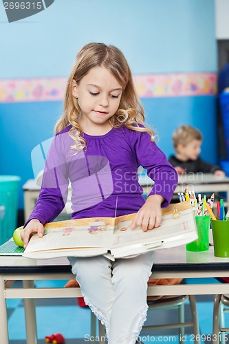 Image of Girl Reading Book While Sitting On Desk At Kindergarten