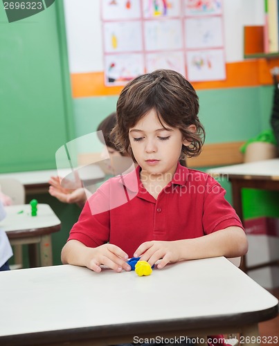 Image of Boy Molding Clay While Friends Playing In Background