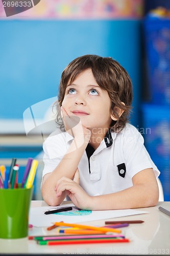 Image of Boy Looking Up While Sitting With Hand On Chin At Desk