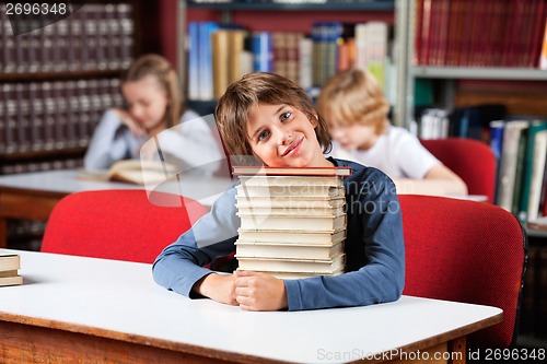 Image of Cute Schoolboy Sitting With On Stack Of Books At Table In Librar