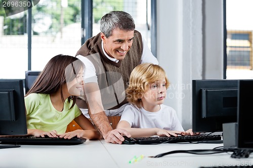 Image of Happy Teacher Assisting Schoolchildren In Using Desktop Pc