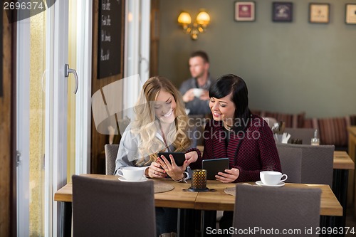 Image of Female Friends Using Digital Tablets At Table