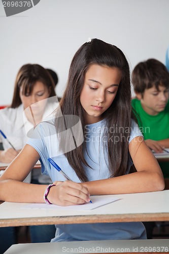 Image of Female Student Writing Paper At Desk In Classroom