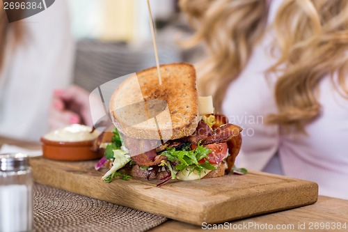 Image of Sandwich On Wooden Plate With Women In Background