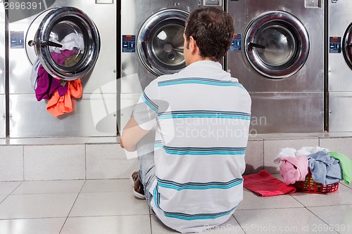 Image of Man Sitting In Front Of Washing Machines