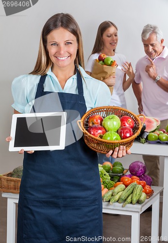 Image of Saleswoman Holding Digital Tablet And Fruits Basket
