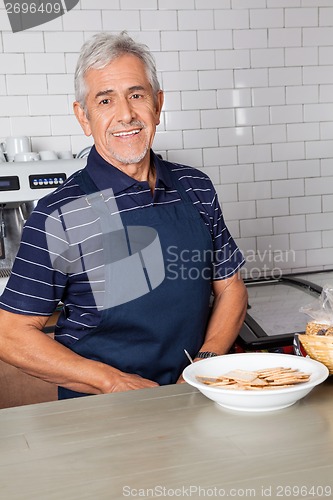 Image of Senior Salesman With Plate Of Biscuits At Counter