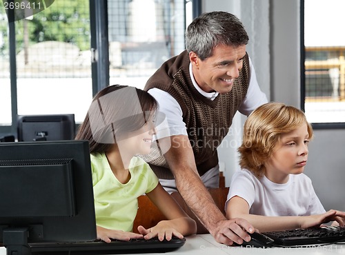 Image of Teacher Assisting Schoolchildren In Using Desktop Pc