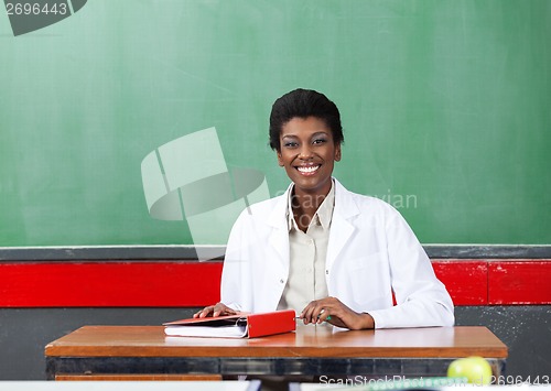 Image of Portrait Of Happy Teacher Sitting At Desk In Classroom
