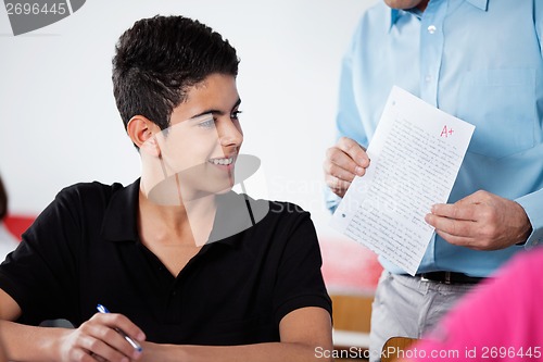 Image of Professor Holding Paper With Teenage Boy At Desk