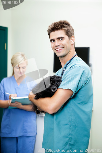 Image of Veterinarian Doctor Carrying A Dog With Female Nurse Writing On