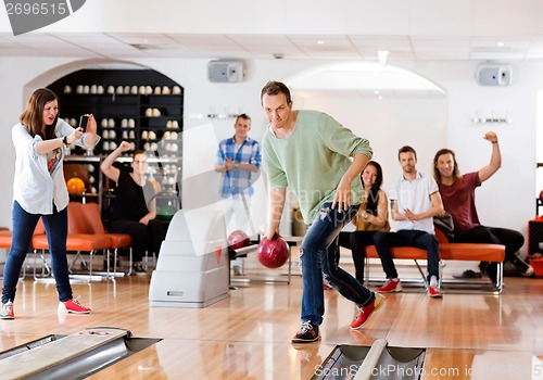 Image of Man Bowling With Friends Cheering in Club