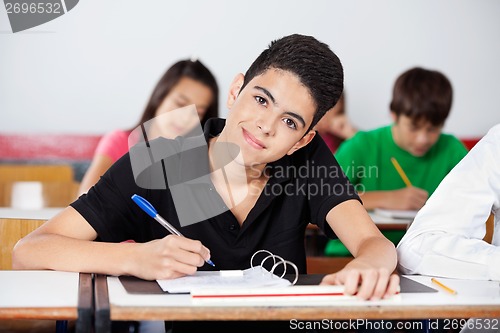 Image of Teenage Boy Writing At In Classroom