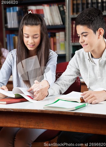 Image of Teenage Couple Reading Book Together In Library