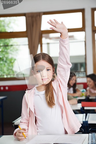 Image of Schoolgirl Raising Hand While Standing In Classroom