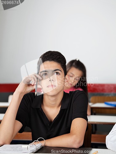 Image of Teenage Schoolboy Looking Away While Sitting At Desk