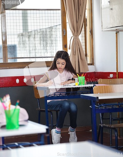 Image of Schoolgirl Writing In Book At Desk In Classroom
