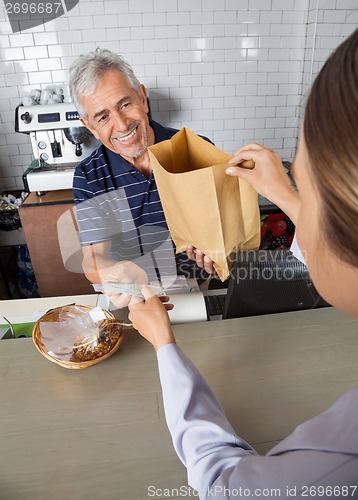 Image of Salesman Collecting Cash While Passing Grocery Bag To Customer