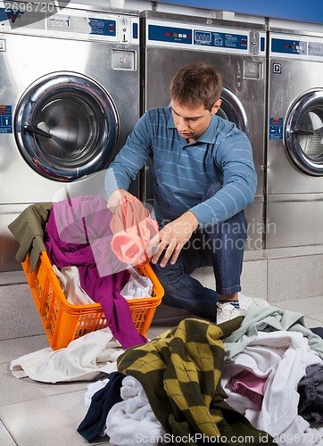 Image of Man Putting Dirty Clothes In Basket at Laundromat