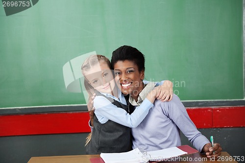 Image of Happy Schoolgirl Hugging Teacher At Desk