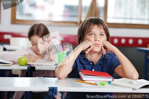 Image of Bored Schoolboy Looking Away Sitting At Desk In Classroom