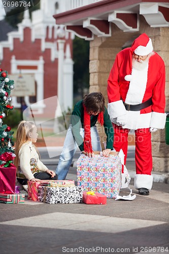 Image of Santa Claus And Girl Looking At Boy Opening Gift