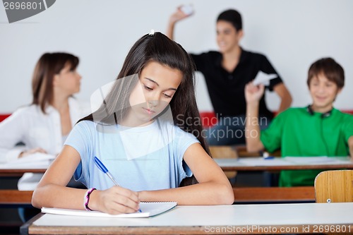 Image of Schoolgirl Writing At Desk While Classmates Playing