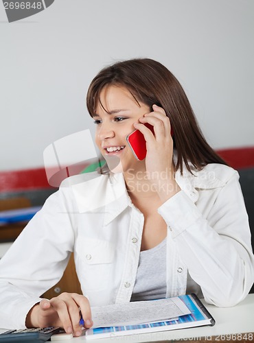 Image of Schoolgirl Looking Away While Using Phone At Desk