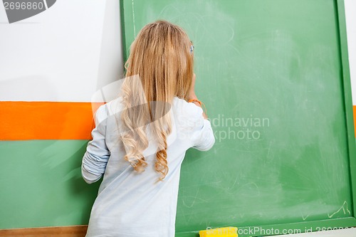 Image of Little Girl Writing On Chalkboard In Classroom