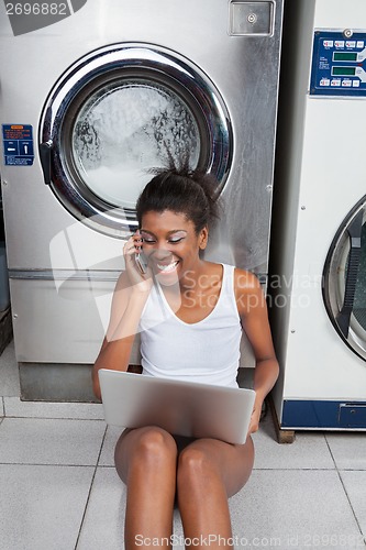 Image of Woman Using Laptop And Mobilephone In Laundry