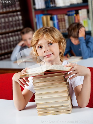 Image of Schoolboy Sitting With Stack Of Books At Table In Library