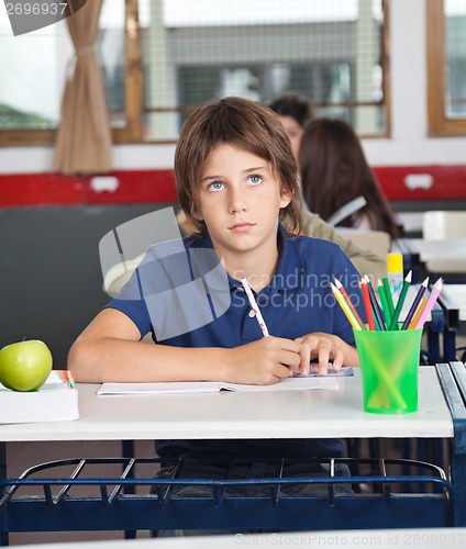 Image of Schoolboy Looking Away While Writing At Desk