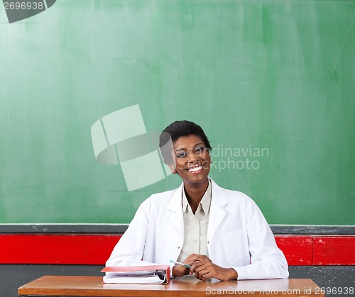 Image of Happy Female Teacher Sitting At Desk In Classroom