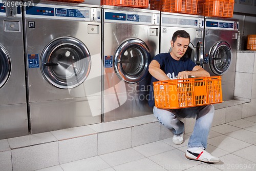Image of Man With Basket Of Clothes Sitting At Laundromat