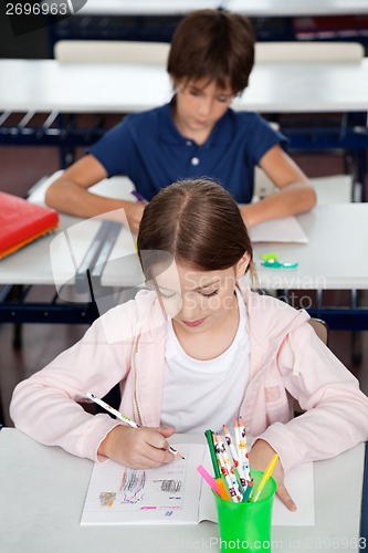 Image of Schoolgirl Drawing At Desk In Classroom
