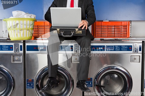 Image of Businessman Using Laptop While Sitting On Washing Machine