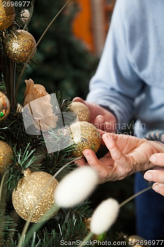 Image of Couple Holding Baubles Hanging On Christmas Tree At Store