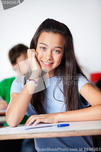 Image of Happy Schoolgirl Sitting At Desk In Classroom