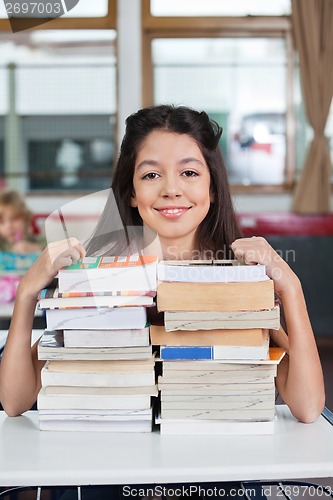 Image of Schoolgirl Smiling With Stacked Books At Desk