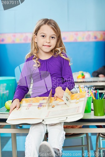 Image of Girl With Book Sitting On Desk In Classroom