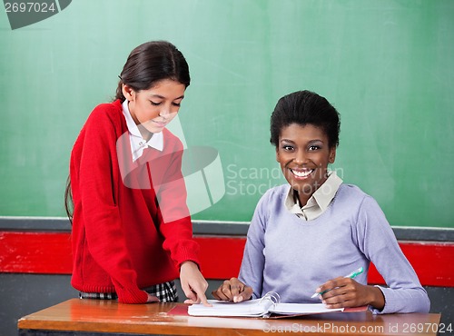 Image of Portrait Of Teacher With Girl Pointing On Binder At Desk