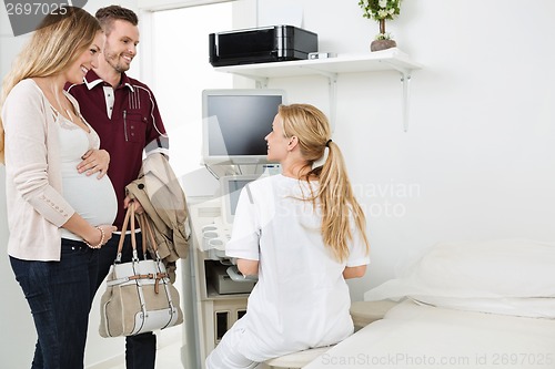 Image of Doctor Looking At Expectant Couple In Clinic
