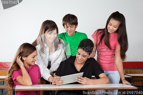 Image of Teenage Schoolboy Showing Tablet To Classmates At Desk