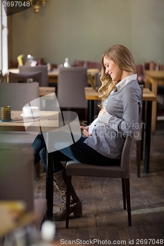 Image of Pregnant Woman Holding Her Belly At Cafe