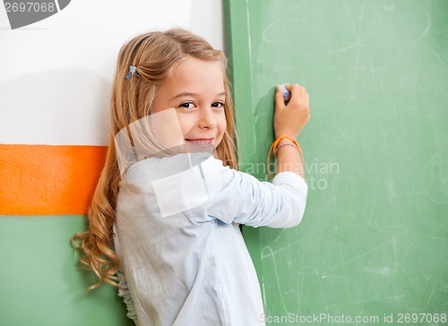 Image of Girl Writing On Green Chalkboard In Classroom