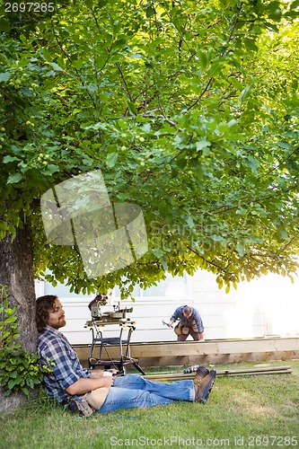 Image of Carpenter With Eyes Closed Leaning On Tree Trunk